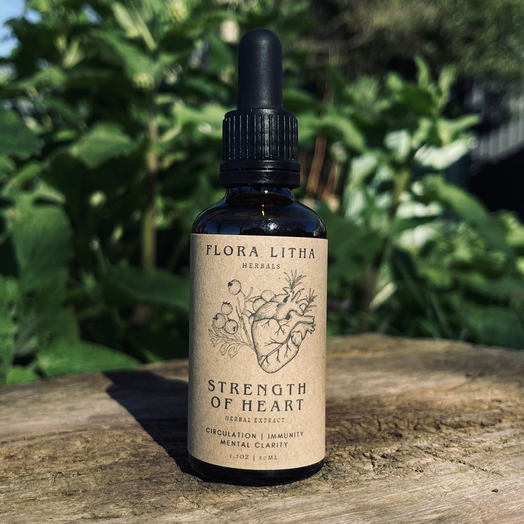 Bottle of Flora Litha Strength of Heart herbal extract on a wooden surface with a natural background