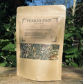 Kraft paper packaging of 'Period Pain Relief' herbal tea on a wooden surface with a natural background.