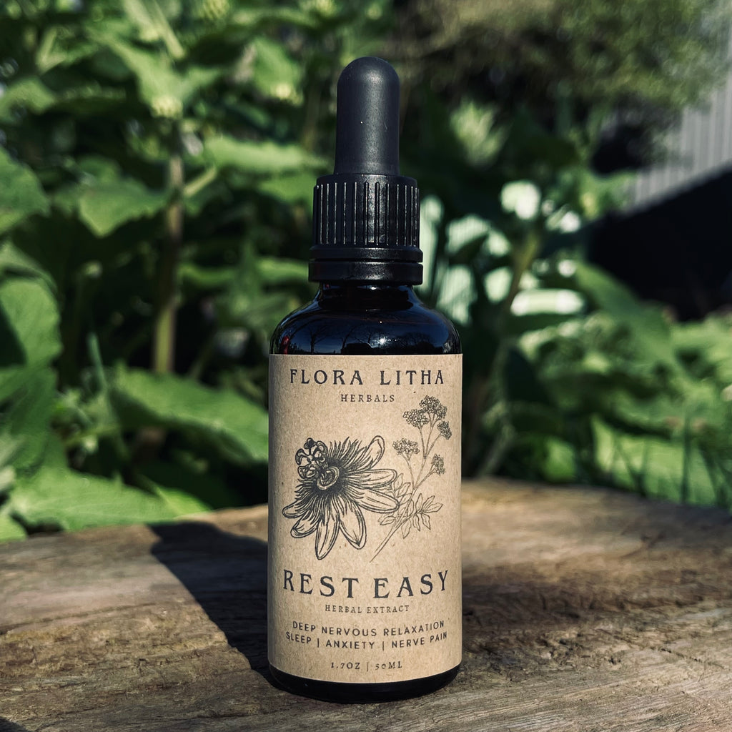 Bottle of Flora Litha Rest Easy herbal extract on a wooden surface with greenery in the background