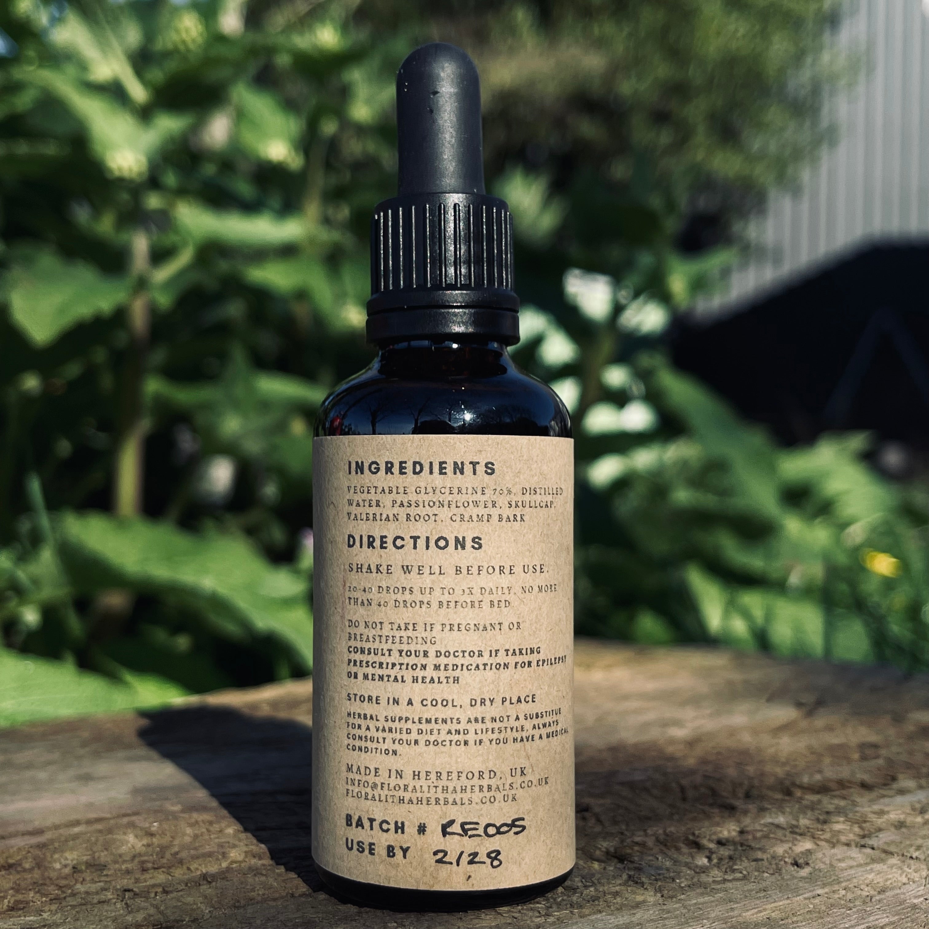 Bottle with dropper on a wooden surface with greenery in the background